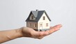 © BENJ - Miniature house model held in hand against white background, symbolizing home ownership, real estate, and housing security.