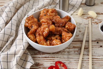Wall Mural - Bowl with tasty sweet and sour chicken on light wooden background, closeup