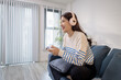 © PHOTO4U - A young woman sits on a sofa wearing headphones while holding a game controller and playing a video game on her laptop. Her cheerful expression shows enjoyment and excitement.