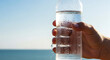 © HADI INCREDIBLE - Man s hand holding a refreshing cold water bottle covered in condensation with the ocean in the background on a sunny day