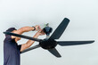 © izzuan - A man installing a ceiling fan. Home improvement, professional work, and technical skill concept.