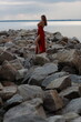© Сергей Луговский - Beautiful slim young woman in long red dress standing on stones at the sea