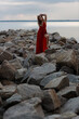 © Сергей Луговский - Beautiful slim young woman in long red dress standing on stones at the sea