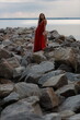 © Сергей Луговский - Beautiful slim young woman in long red dress standing on stones at the sea