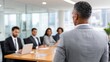 © Moopingz - A man in a suit addresses a group of diverse professionals seated at a conference table in a modern office meeting room.