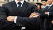 © lililia - A businessman poses confidently with arms crossed, surrounded by colleagues in uniforms in a modern office environment
