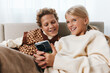 © SHOTPRIME STUDIO - Authentic moment of children sharing a playful screen moment on a cozy couch, casual home setting, soft lighting, warm sweaters, relaxed lifestyle and genuine interaction.