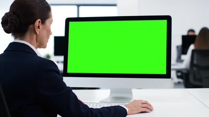Woman concentrating on computer with green screen display creating content in a modern office environment