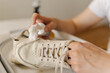 © dikushin - Close-up process of cleaning white sneakers with scrubbing brush and detergent, removing stubborn stains from footwear in basin, preserving shoe hygiene and appearance thorough washing work.