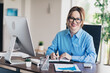 © deagreez - Professional businesswoman working in a modern office with a computer and documents, smiling confidently at the camera