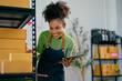 © Parichat - Smiling african american female business owner using digital tablet and checking parcels on shelves in her storehouse