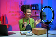 © Parichat - Happy african american woman presenting product for sale online using smartphone with ring lamp
