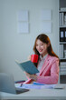 © PaeGAG - Young Asian manager enjoying a coffee break while reviewing her notes at her desk