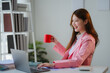 © PaeGAG - Young Asian businesswoman drinking coffee and working on laptop in office