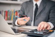 © khunkornStudio - Calculator accounting Manager calculates numbers at desk with laptop and smartphone in office, tracking data, budget, expense, revenue, profit, audit to guide strategy.