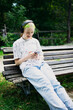 © Анна Молько - Teen girl with bright green hair smiling while looking at smartphone and listening to music in black headphones. Sitting on a bench in the park, enjoying leisure and modern lifestyle