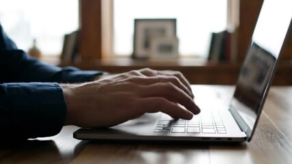 A professional businessman's hands typing on a modern laptop keyboard while working remotely from a home office on a project researching digital technology and communication