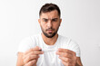 © Prostock-studio - Sad shocked young male with beard looks at thermometer with high temperature and suffering from ill alone in bedroom interior. Disease, health problems, influenza, flu and covid-19 virus, free space
