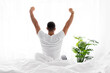 © Prostock-studio - Happy young caucasian muscular man sits on white bed, wake up, stretching body in bedroom interior and looks at window, back, sun flare. Relax at home, guy enjoy good morning during covid-19 lockdown