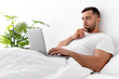 © Prostock-studio - Busy serious concentrated millennial muscular european man typing on computer, create idea, searching info, lies on bed in bedroom interior. Business and work at home, freelance due covid-19 lockdown