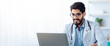 © Prostock-studio - Online remote consultation of patient , modern telemedicine, health care. Young friendly arabic male doctor with beard in glasses, in white coat, looks at laptop, makes notes in office interior