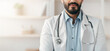 © Prostock-studio - Doctor online, health care remotely, telemedicine during covid-19 lockdown. Young arabian handsome bearded man in white coat with stethoscope looks at camera in office interior in clinic, empty space