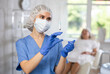 © JackF - Female doctor holding syringe in medical mask and gloves, for injecting the vaccine into patient who is sitting behind.