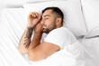 © Prostock-studio - Calm millennial handsome guy with beard sleeps on white comfortable bed on soft pillow in bedroom, top view, profile. Rest and relaxation at home, health care and sleep at night, free space, close up