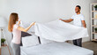 © Prostock-studio - Cheerful multiracial couple making bed in morning, having fun at home. Loving young family wearing pajamas, doing house chores together, cleaning up in bedroom after sleeping