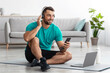 © Prostock-studio - Cheerful millennial caucasian man in headphones sits on mat on floor typing on smartphone, with computer in living room interior. New normal, remote training and technology for sports, video call