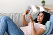 © Prostock-studio - Enjoy spare time alone lying on sofa watching news on phone, comfortable, relaxing at home, using tech. Glad young black woman typing on smartphone, surfing in internet in living room interior
