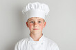 © VICHIZH - Young chef in white uniform and hat stands against a plain backdrop with a calm, focused expression, signaling curiosity, discipline, and early culinary dreams.