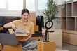 © Natee Meepian - Online Shopping. Happy woman unboxing clothing while live streaming.