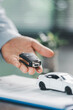 © doidam10 - Business office, woman employee finalizes deal with client, handing over car key after signing contract and reviewing insurance and loan documents for sale or rent of vehicle at table.