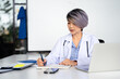 © Fahng - Woman doctor therapist writing in medical journal, sitting at table with stethoscope in office, working with documents, physician writing illness history,