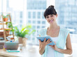 Female professional holding tablet standing in bright office with laptop and plants, copy space