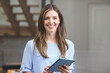 © wavebreak3 - Woman standing in office wearing blue blouse holding tablet near wooden staircase and panel door