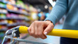 © AucArtStudio - Consumer confidence in everyday shopping captured by close up hand on yellow cart handle in supermarket aisle showing purchase decision and focus