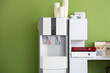 © Pixel-Shot - Modern water cooler with paper cups and workplace near green wall