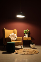 Poster - interior of stylish living room with cozy brown armchair, houseplant and glowing lamp at night