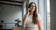 © Sulfabndi - Happy young businesswoman talking on phone near window in modern office smiling confident successful entrepreneur