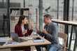 © Tj - Two smiling business partners giving thumbs up while celebrating success, sitting at a desk in a modern office, surrounded by a laptop and important documents, radiating positivity and teamwork