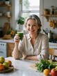© Ira - Happy mature woman enjoying natural green detox shot sitting at bright kitchen surrounded by fresh fruits and herbs, authentic healthy lifestyle photography scene