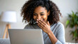 © Gunawan - Smiling woman laughing while looking at her laptop screen, covering her mouth with her hand in amusement at a home setting