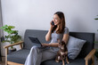 © Wasana - A woman is sitting on a couch talking on her cell phone while her dog is laying