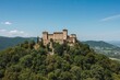 A fortified military stronghold perched atop a densely forested mountain near a mountaintop village