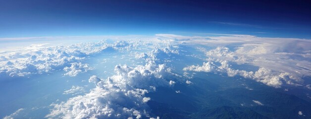 Wall Mural - Aerial view capturing fluffy white clouds with sunlight piercing through them above a landscape of green rolling hills and a brilliant blue sky