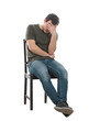 © 1STunningART - Disappointed and pessimistic young man sitting on a chair covering face with his palm. Desperate guy seated alone suffer anxiety, distress depression feeling, full length portrait isolated