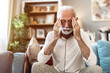 © Jelena Stanojkovic - Stress, headache and senior man in home with worrying, overthinking or mental health. Anxiety, mistake and elderly male person with migraine in living room for regret, vertigo or brain fog in house.