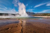 Morning eruption of a hot spring in a barren landscape with steam rising, water, and a clear sky